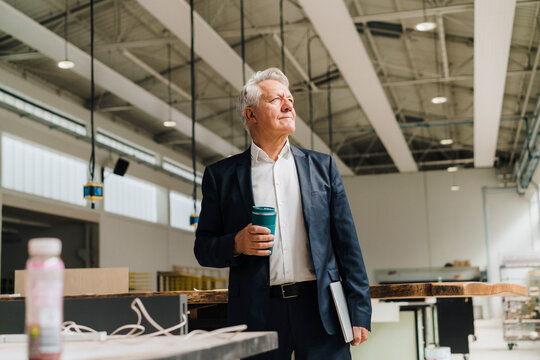 Thoughtful businessman holding reusable cup in factory