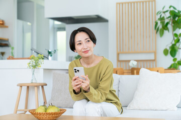 リビングでスマホを見るミドルの女性