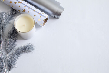 Flat lay of a white candle, silver star wrapping paper, and silver tinsel garland on a clean white background. Elegant holiday or New Year theme with space for text or product placement.