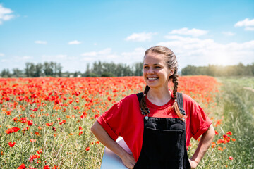 Happy young woman standing in blooming red poppy field promoting nature restoration and biodiversity