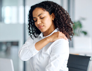 Young woman massaging her own shoulder, work-related pain, professional setup, plain white shirt