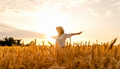 Happy woman with outstretched arms enjoying sunset in grain field in summer