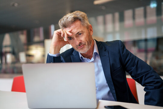 Stressed mature businessman using laptop at table in cafeteria