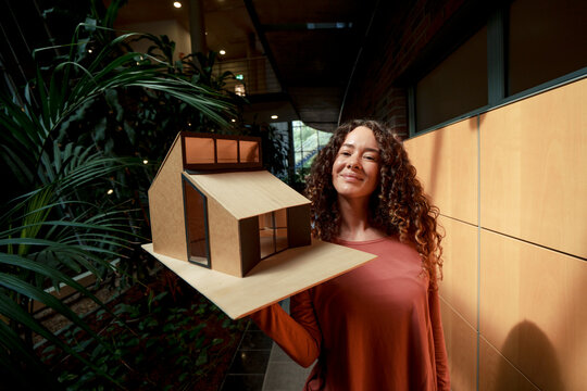Smiling young architect with model house in office
