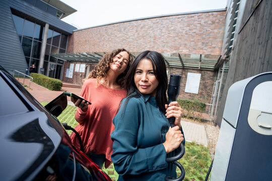 Woman with electric plug by friend holding smart phone