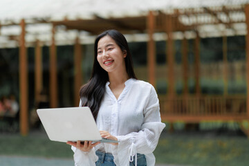 Smiling asian freelancer working remotely with laptop outdoors