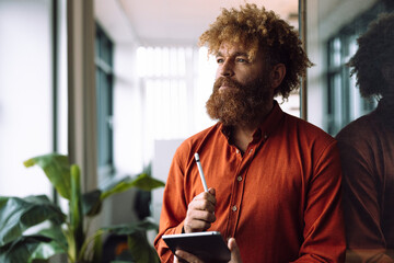 Thoughtful businessman holding tablet PC with digitized pen in office