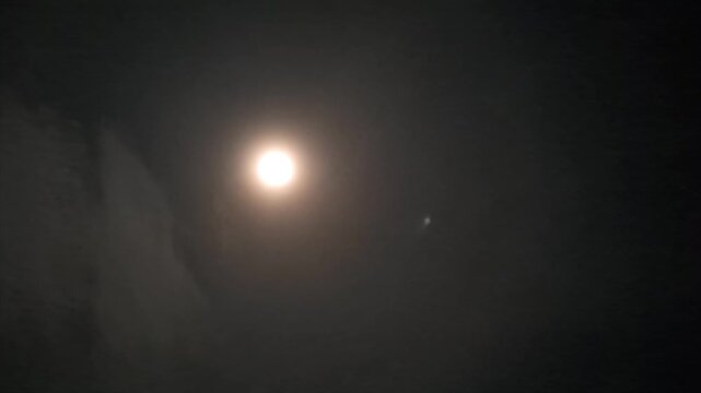 Atmospheric footage of a bright full moon glowing in the dark night sky.