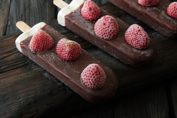 Concept, creamy ice cream on a stick in chocolate glaze, on an old wooden table. On top of the ice...