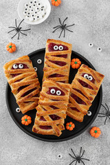 Halloween mummies pies with cherry filling and sugar eyes on a gray concrete background. Funny food idea. Holiday dessert. Top view.