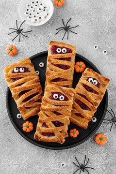 Naklejki Halloween mummies pies with cherry filling and sugar eyes on a gray concrete background. Funny food idea. Holiday dessert. Top view.