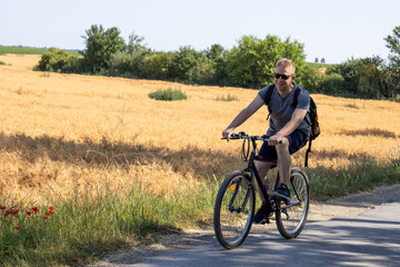 man cycling toward camera wearing sunglasses with tree shadows on road

