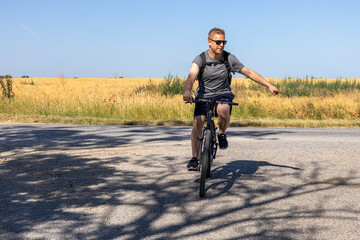 man signaling turn on rural road while cycling in summer landscape