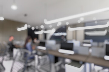 Fototapeta premium Blurred modern office interior with open space design. Rows of workstations and minimalistic lighting fixtures create a contemporary business environment.