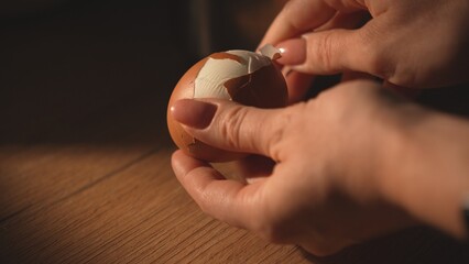 Hands peeling boiled brown egg on wooden table close-up