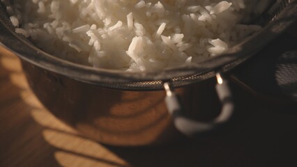 Cooked white rice in metal pot on wooden surface