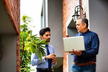 Asian corporate professionals with laptop walking brainstorming outside contemporary office