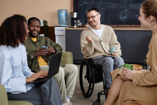 Smiling business people siting with coffee cups and having discussion in office