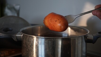 Cook checks boiled unpeeled potato with fork over kitchen pot