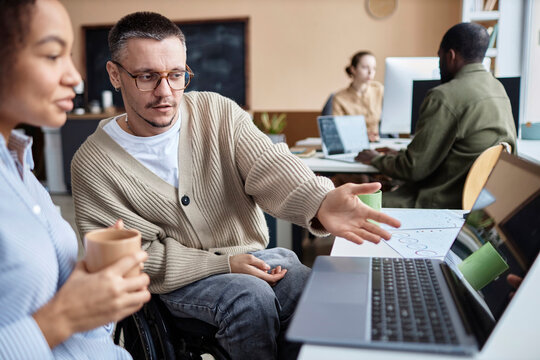 Businessman with disability having discussion over new computer software on laptop with businesswoman at desk