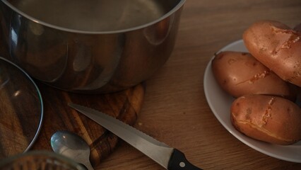 Dolly shot of cooked unpeeled potatoes with pot and knife on table