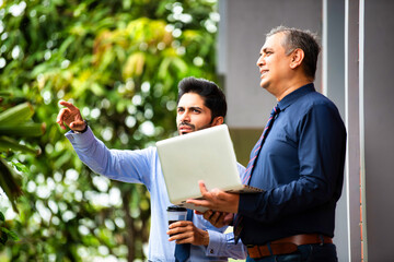 Asian corporate professionals with laptop walking brainstorming outside contemporary office