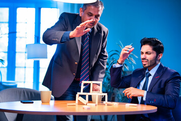 Young Indian corporate workers laugh as wooden block tower collapses in office game