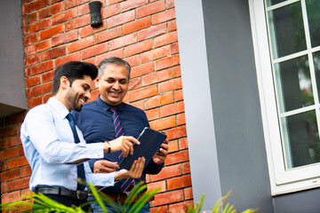 Indian corporate professionals walk with tablet, engaged in discussion outside office building
