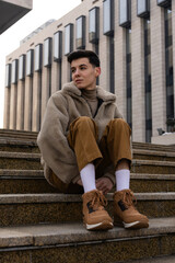 Young man sitting on stairs wearing casual winter clothes.
