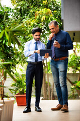 Indian corporate professionals walk with tablet, engaged in discussion outside office building