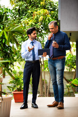 Indian corporate professionals walk with tablet, engaged in discussion outside office building