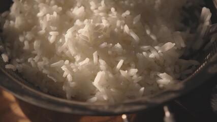 Dolly shot of cooked white rice in metal pot on wooden surface