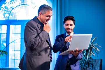 Indian business partners review data together using laptop in contemporary corporate office