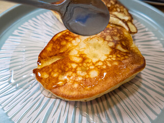 pancakes and honey Pour syrup over pancakes from silver syrup pitcher. Homemade pancakes in a gray plate are poured with a thin stream of slow motion honey. Medium plan.