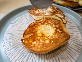 pancakes and honey Pour syrup over pancakes from silver syrup pitcher. Homemade pancakes in a gray plate are poured with a thin stream of slow motion honey. Medium plan.