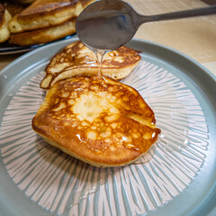 pancakes and honey Pour syrup over pancakes from silver syrup pitcher. Homemade pancakes in a gray plate are poured with a thin stream of slow motion honey. Medium plan.