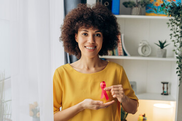 Smiling Latin woman showing pink ribbon for breast cancer awareness
