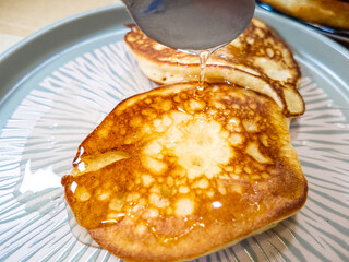 pancakes and honey Pour syrup over pancakes from silver syrup pitcher. Homemade pancakes in a gray plate are poured with a thin stream of slow motion honey. Medium plan.