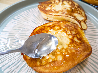 pancakes and honey Pour syrup over pancakes from silver syrup pitcher. Homemade pancakes in a gray plate are poured with a thin stream of slow motion honey. Medium plan.