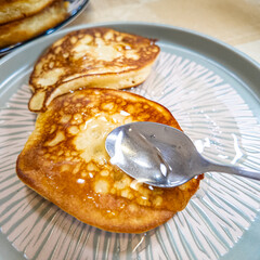 pancakes and honey Pour syrup over pancakes from silver syrup pitcher. Homemade pancakes in a gray plate are poured with a thin stream of slow motion honey. Medium plan.