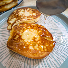 pancakes and honey Pour syrup over pancakes from silver syrup pitcher. Homemade pancakes in a gray plate are poured with a thin stream of slow motion honey. Medium plan.