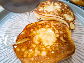 pancakes and honey Pour syrup over pancakes from silver syrup pitcher. Homemade pancakes in a gray plate are poured with a thin stream of slow motion honey. Medium plan.