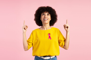 Woman showing pink ribbon and pointing up for breast cancer awareness