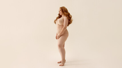 Confident woman with long red hair posing against neutral background. Concept of body positivity, powerful femininity, stylish bodywear, fashion confidence, bold character in underwear marketing.