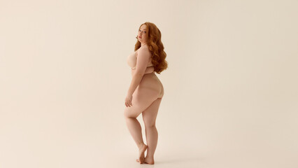 Confident plus-size woman posing in nude lingerie with neutral backdrop. Concept of expressive...