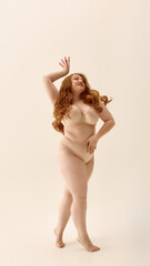 Confident woman with red hair posing in beige underwear on a neutral background. Concept of...