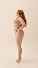 Confident plus-size woman standing in profile on neutral background. Concept of relaxed identity,...