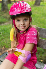 Little girl in a protective pink helmet, wearing protective pink elbow pads for safe roller skating...