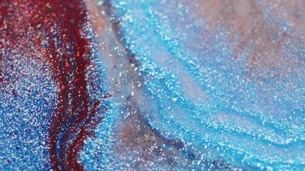 A macro shot captures red and blue glitter as water is injected and flows through, displacing the particles in shimmering motion.