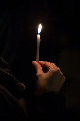 A person is holding a lit candle in their hand while standing in the dark